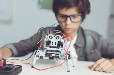 Gözlüklü küçük inek bir robot tutuyor. Onun yaratılması dikkatle bakıyor