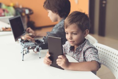 iki erkek atölye masada oturuyor. Bunlardan biri ikinci bir tablet ile bir dizüstü bilgisayar oturuyor.