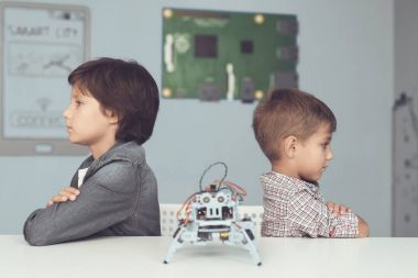 İki erkek gri bir masada poz olan. Aralarında gri bir robottur