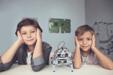 İki erkek gri bir masada poz olan. Aralarında gri bir robottur