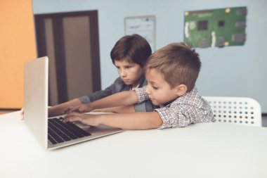 İki erkek masada oturuyor. Onlardan biri gri bir dizüstü bilgisayar önünde oturuyor. İkinci bir laptop ulaşır