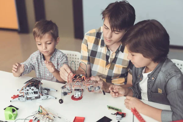 Een jonge kerel en twee jongetjes zijn het verzamelen van robots. Om hen heen zijn delen van verschillende robots en mechanismen — Stockfoto