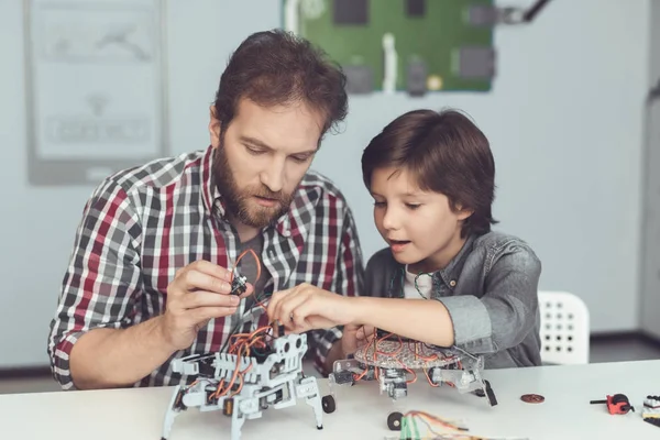 Een man helpt een jongen met een robot-vergadering. De jongen kijkt aandachtig als een man een robot verzamelt — Stockfoto