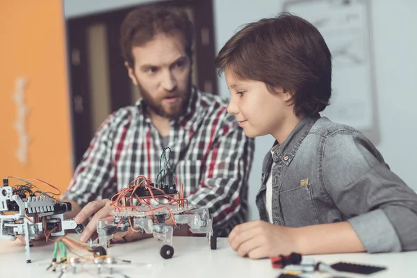 Een man helpt een jongen met een robot-vergadering. De jongen kijkt aandachtig als een man een robot verzamelt — Stockfoto