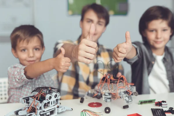 Молодий хлопець і двоє маленьких хлопчиків збирають роботів. Вони показують великі пальці вгору — стокове фото