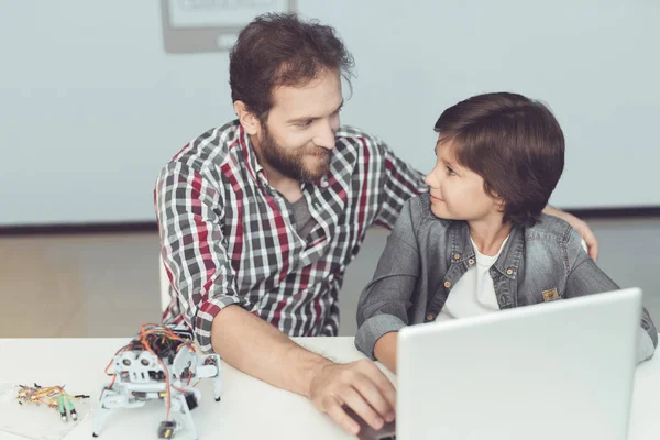 Um homem ajuda um rapaz com uma montagem de robôs. Eles se sentam na frente do laptop e estão se preparando para programar o robô — Fotografia de Stock