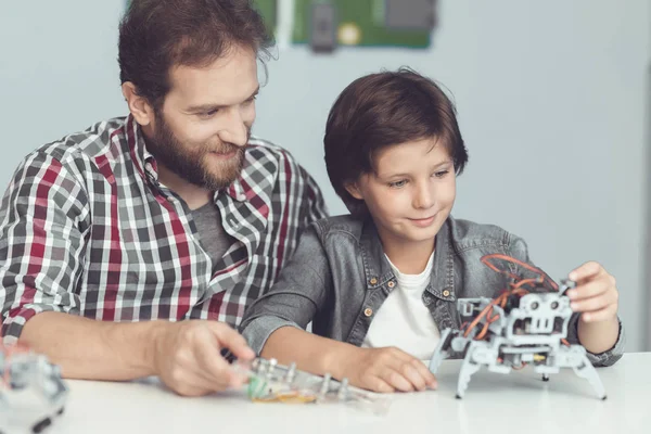 Een man helpt een jongen met een robot-vergadering. Een man horloges als de jongen afwerkingen monteren van de robot — Stockfoto