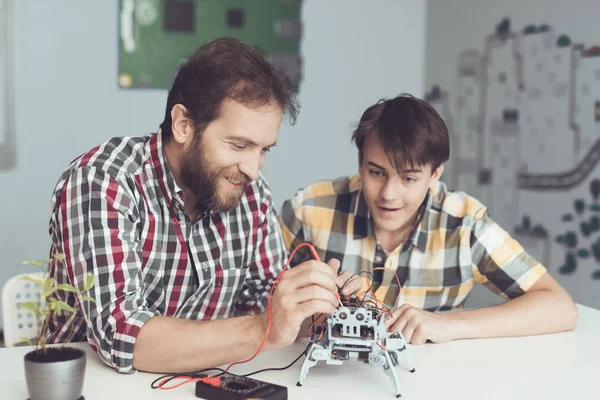 Um cara jovem olha com prazer como um homem realiza medições de controle do desempenho do robô — Fotografia de Stock
