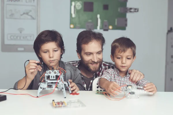 Um homem e dois rapazes constroem um robô. O homem ajuda os meninos com a montagem — Fotografia de Stock