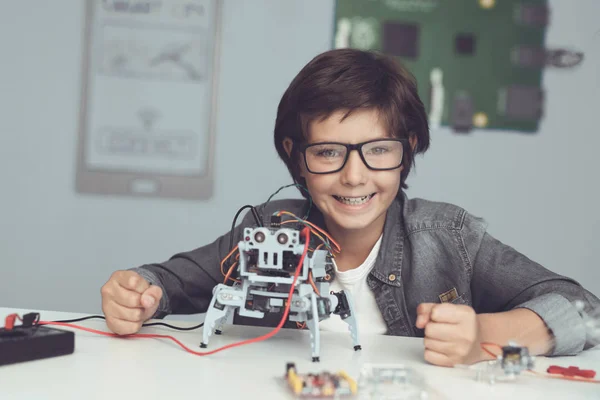 Een kleine nerd in glazen is het bezit van een robot. De jongen kijkt zeer tevreden — Stockfoto