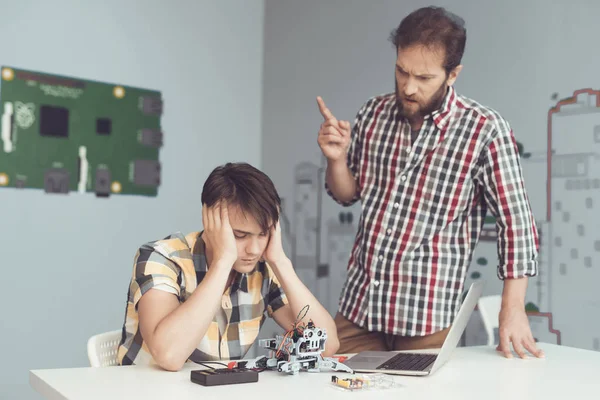 Muž kárá teenagera, který zlomil robotovi. V pubertě se sedí u stolu s hlavou v dlaních — Stock fotografie