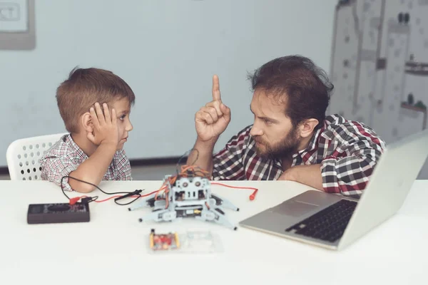 De jongen kwetsen de robot. Een man chastises ernstig de jongen, uit te leggen aan hem zijn fouten — Stockfoto