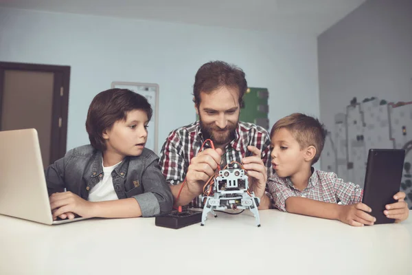 Zwei Jungen arbeiten an Tablet und Laptop, dazwischen sitzt ein Mann und konstruiert einen Roboter — Stockfoto