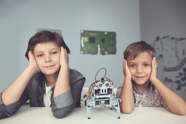 Two boys are posing at a gray table. Between them is a gray robot — Stock Photo, Image