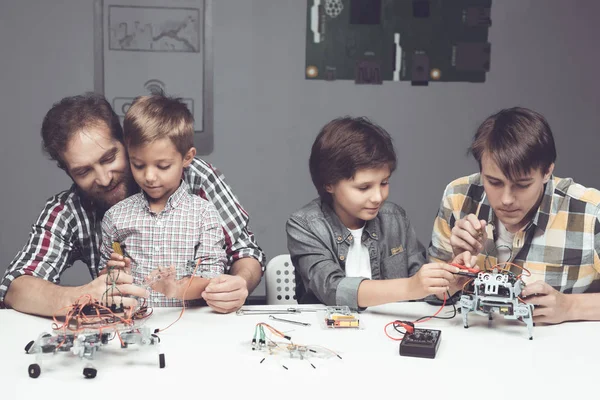 Dois meninos um adolescente e um homem adulto estão sentados na oficina e construindo um robô — Fotografia de Stock