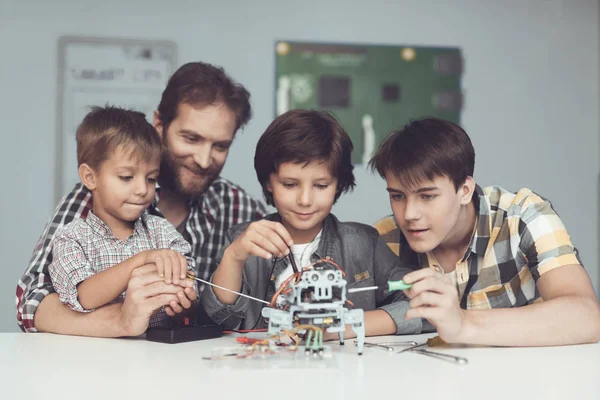 Twee jongens een tiener en een volwassen mannelijke zijn zittend in de werkplaats en de bouw van een robot — Stockfoto
