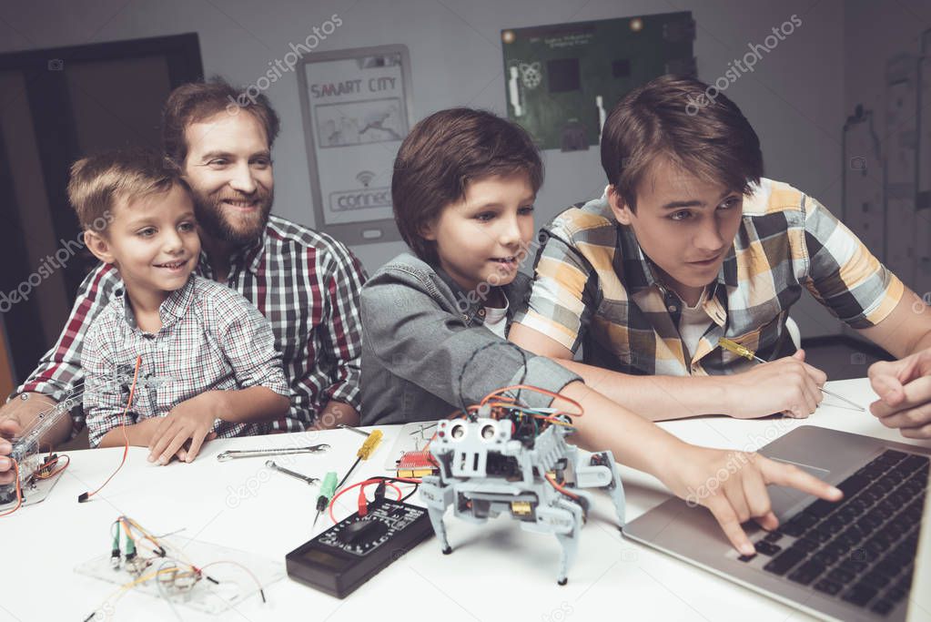 Two boys a teenager and an adult male are sitting in the workshop and constructing a robot