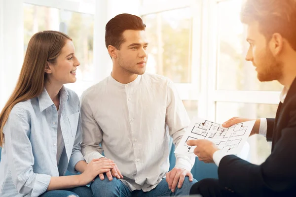 Um jovem casal numa reunião com um agente imobiliário. Guy e menina fazem um contrato com corretor de imóveis comprando propriedade . — Fotografia de Stock