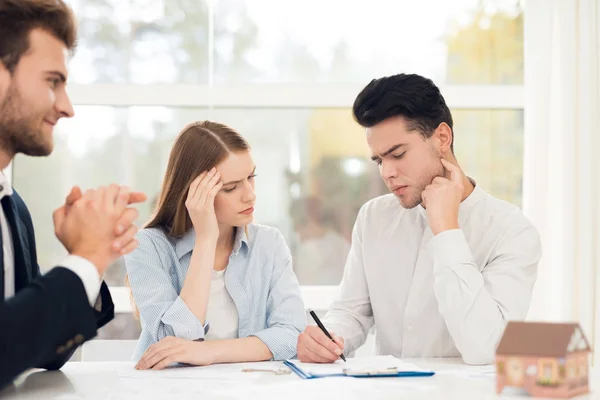 Pareja joven en una reunión con un agente inmobiliario. Guy y chica hacen un contrato con un agente inmobiliario comprando una propiedad . — Foto de Stock