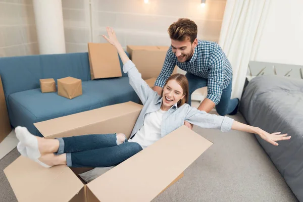 Young couple having fun while moving to new apartment. Moving newlyweds. Girl is sitting in a box. — Stock Photo, Image