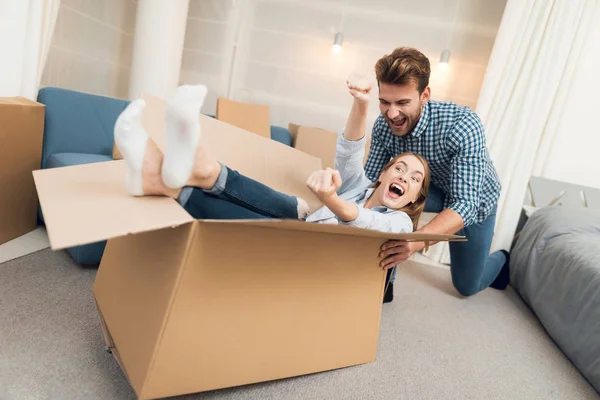 Unga par att ha kul medan du flyttar till ny lägenhet. Rörliga nygifta. Flickan sitter i en låda. — Stockfoto