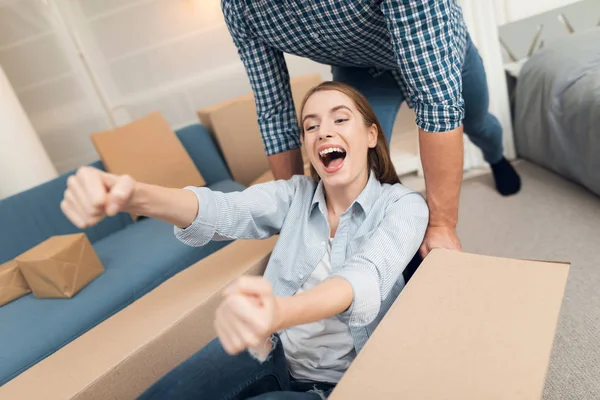 Young couple having fun while moving to new apartment. Moving newlyweds. Girl is sitting in a box. — Stock Photo, Image