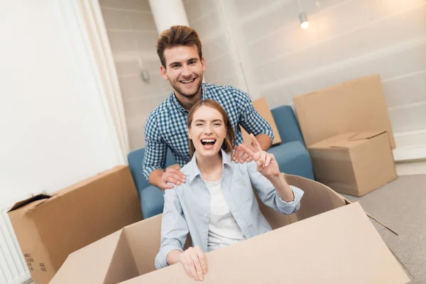 젊은 커플 새 아파트에 이동 하는 동안 재미. 신혼 부부를 이동합니다. 여자는 한 상자에 앉아. — 스톡 사진