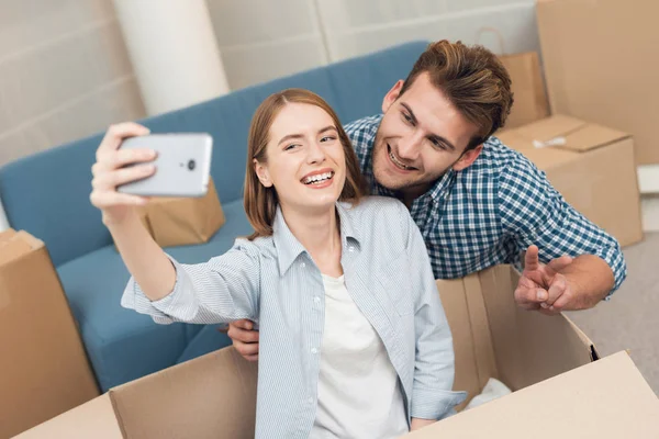 A young couple makes selfie while moving to a new apartment. Moving newlyweds to new housing. — Stock Photo, Image