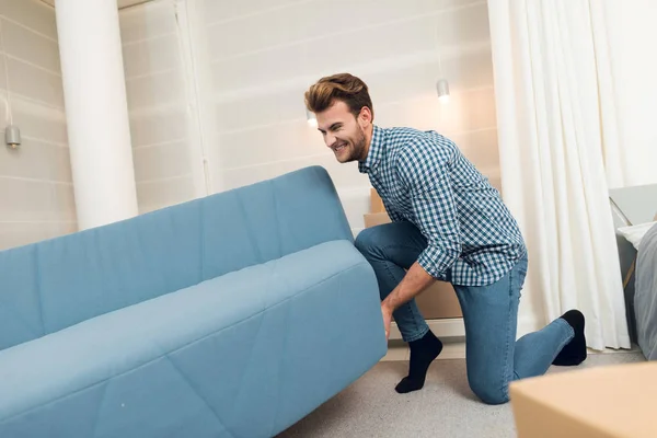 The guy moves the sofa while moving to a new home. The guy does a reshuffle in the room. — Stock Photo, Image