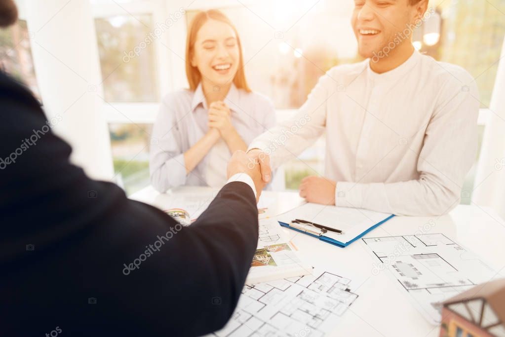 Young couple in a meeting with a realtor. A guy and a girl make a contract with a realtor about buying a property. A successful deal with a realtor. The client shakes hands with the realtor.