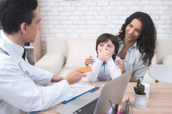 A little boy does not want to take pills, which the doctor gives him.