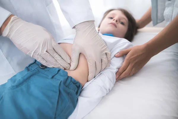 O médico de luvas brancas massageia a barriga de um menino doente . — Fotografia de Stock