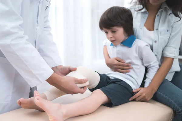 El médico con guantes blancos rebobina la pierna del niño con una venda . — Foto de Stock