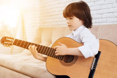 Beyaz bir gömlek küçük bir esmer çocuk gitar çalıyor. Çocuk kendini gitar çalmak öğrenir. Parlak bir room.x içinde kanepede oturuyor