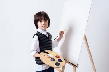 Küçük çocuk sanatçı meslek mastering. Esmer çocuk şövale üzerinde çizer. O boya ve fırça elinde tutuyor.