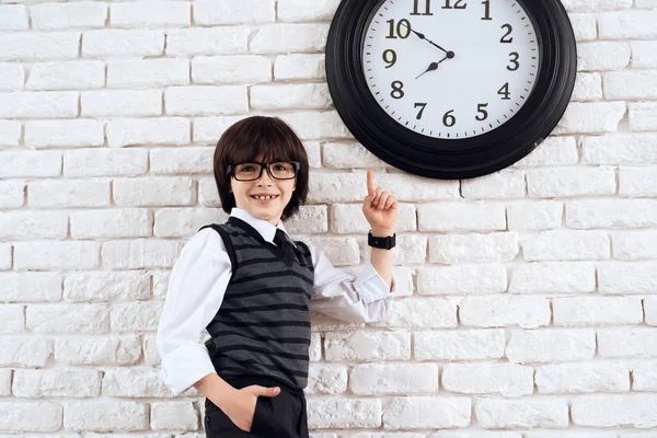 Tmavovlasý Chlapec Stojí Bílé Zdi Obleku Poukazuje Nástěnné Hodiny Malé — Stock fotografie
