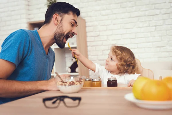 A man spends time with his son. The father of boy is engaged in raising child. Baby is feeding his father. The boy is having breakfast with his father.