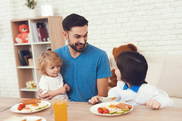 Человек проводит время со своими сыновьями. Отец двух мальчиков занимается воспитанием детей. Отец кормит своего сына. Дети завтракают с отцом
.
