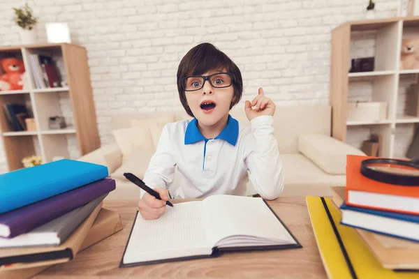 那个男孩正坐在他的作业上 戴眼镜的男孩沉思着 坐在桌子旁 桌子上有课本和练习本 — 图库照片