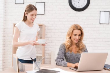 Kızı Anne çay bir fincan getirdim. Bir kadın bilgisayarda çalışıyor. O kız ona yardımcı olur çok memnun oldu. O gülümsüyor.