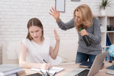 Kızı okul ödevi düzgün yapamaz. Kadın bu yüzden kızgın. O kızı çığlıklar ve bir şişe alkol elinde tutan.