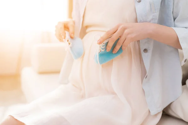 A pregnant girl holds shoes for a newborn. — Stock Photo, Image