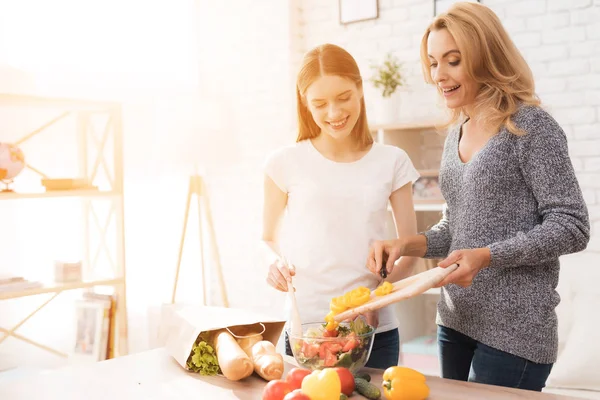 Mom and daughter are cooking together in the kitchen. They use vegetables for cooking. They are in a good mood. They are happy to be together.