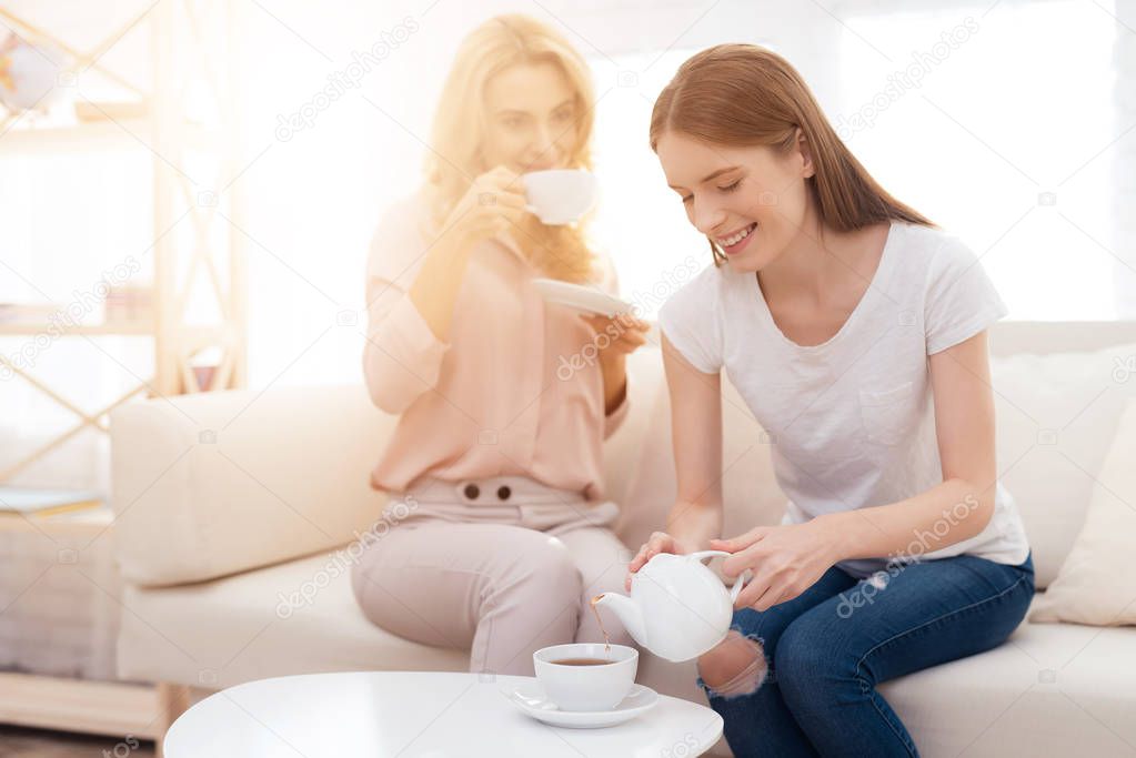 Mom and daughter-teen drink tea. They are sitting on the couch at home. They are in a good mood. They are happy with each other.