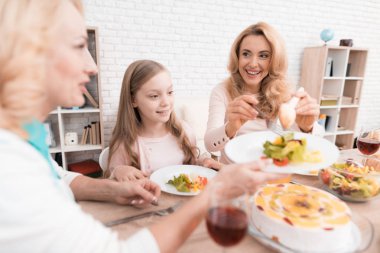 Anne, Büyükanne ve küçük kız birlikte evde yemek yiyorlar. Onların masaya sebze ve tatlılar ellerinde.
