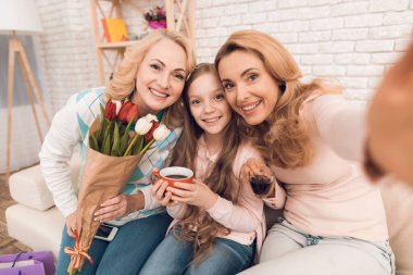 Anne, Büyükanne ve küçük kız kanepede oturan selfie musun. Olgun kadın lale onun elinde vardır..