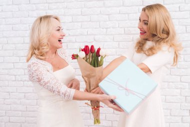 Yetişkin anne ve kızı Kameranın hafif bir duvara yakın birlikte poz olan. Ellerinde çiçekler. Onlar gülüyor.