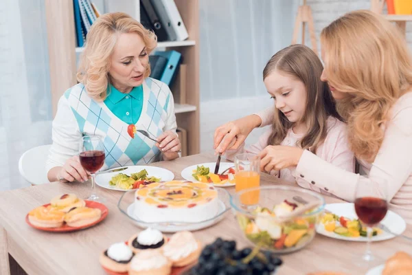 Mom and little girl cut vegetables together in a plate. They have dinner at home. They have vegetables and sweets on their table.