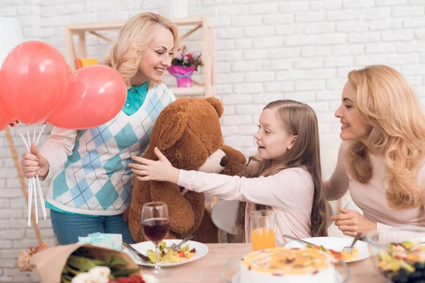 Mom and grandmother give a little girl a big toy bear. They make her a surprise. The family has dinner at home - they have a holiday.
