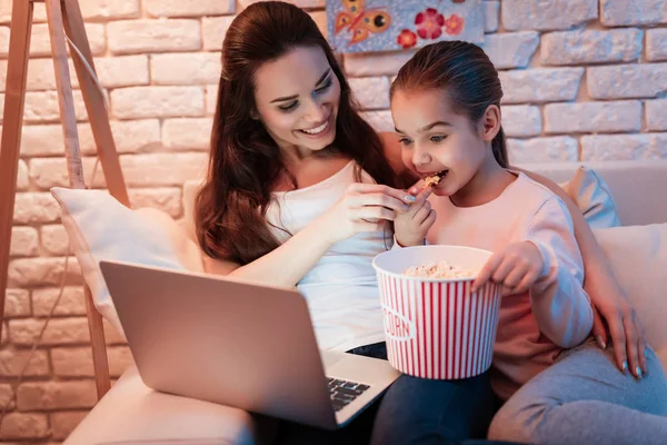 母亲和小女儿看电影在笔记本电脑和吃爆米花在晚上在家 — 图库照片